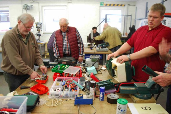 Hier sehen wir mehrere Teilnehmer*innen die gerade in einer Werkstatt etwas Reparieren 