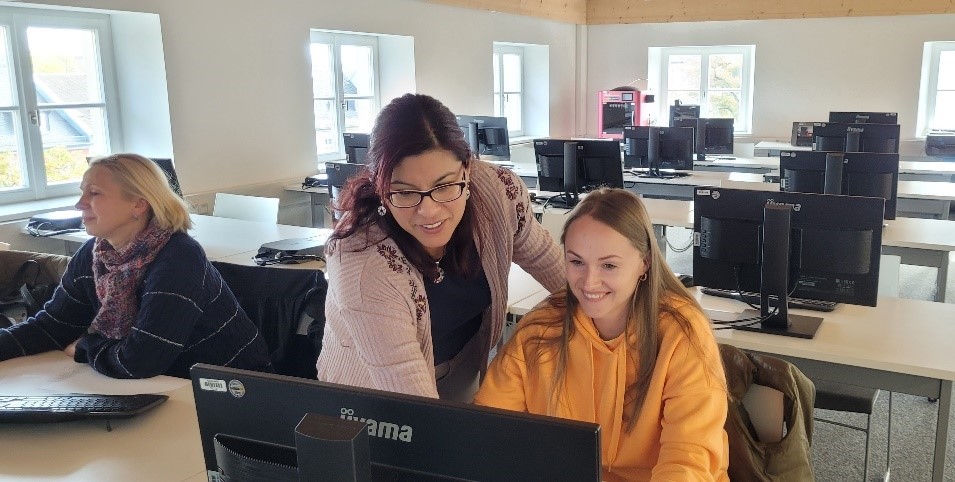 Frau beugt sich zu Schülerin am PC zur Betreuung